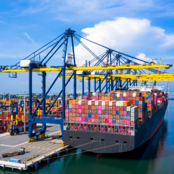 Container de carga sendo descarregado em porto, representando o comércio internacional e importação de produtos.
